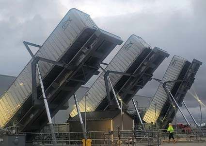 Three large Plainfield Trucking trailers tilted upward, with a person walking nearby at the facility.